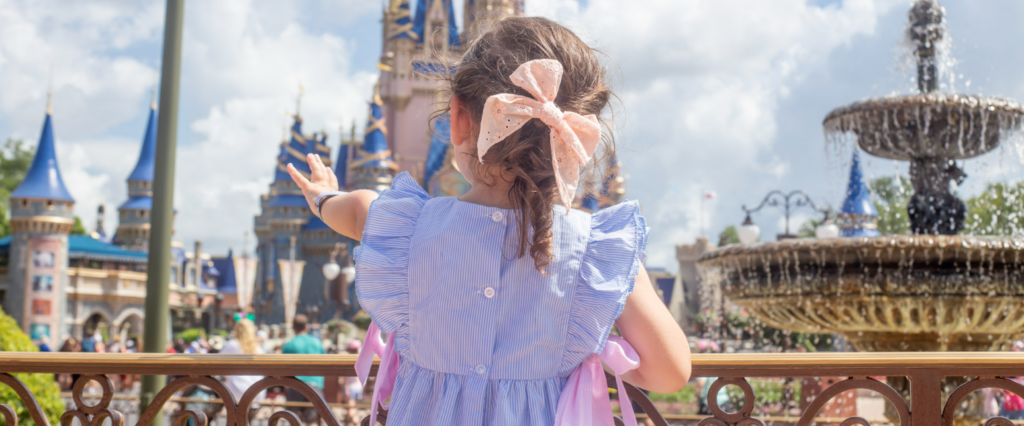 An image of a girl in purple dress extending her arm out to the Castle at Disneyland in Paris
